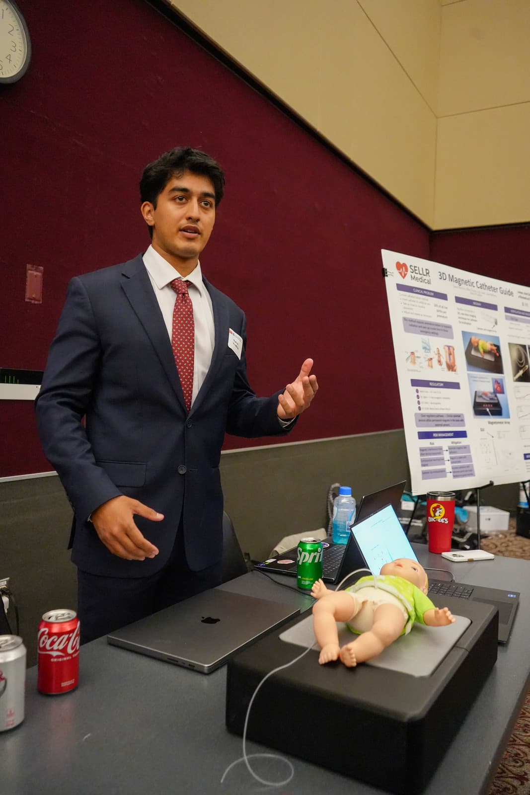 A senior design student presents his team's device at their booth at the 2026 Design Symposium