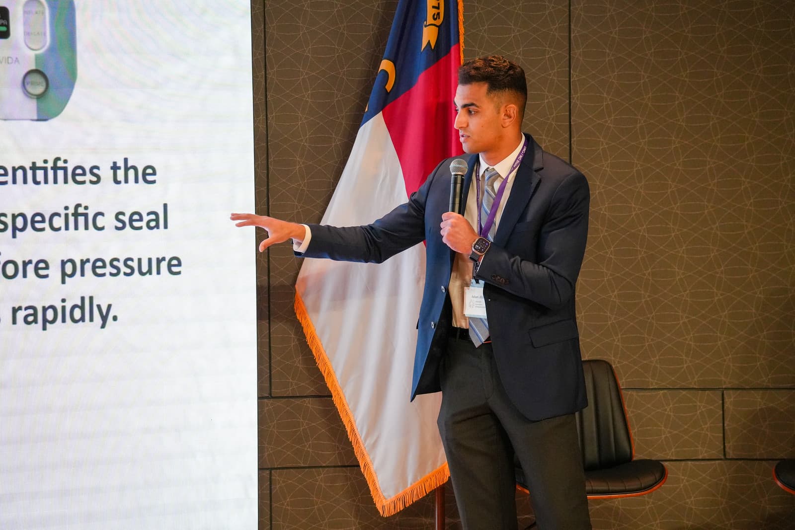 A MedTech venture presenter points to his slide on stage in the NC Biotechnology Center auditorium at the 2026 Showcase